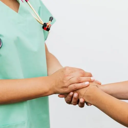 Caregiver in scrubs holding a patient’s hands